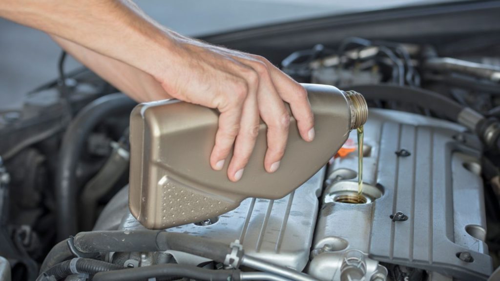 Man pouring a bottle of conventional oil to the engine