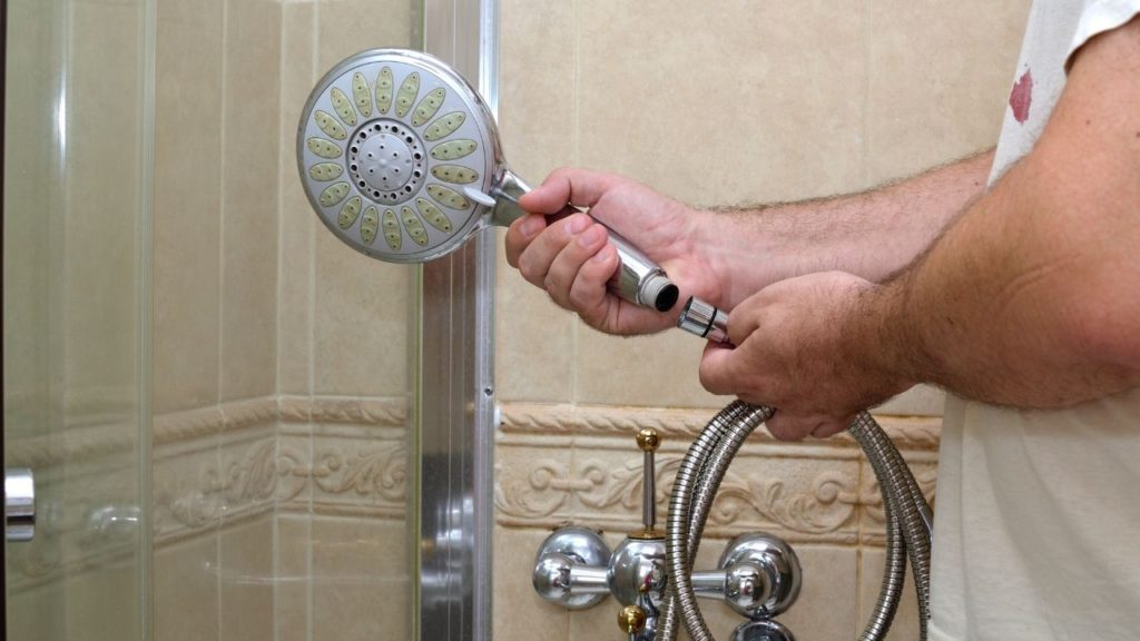 Man removing a dirty handheld showerhead from the hose