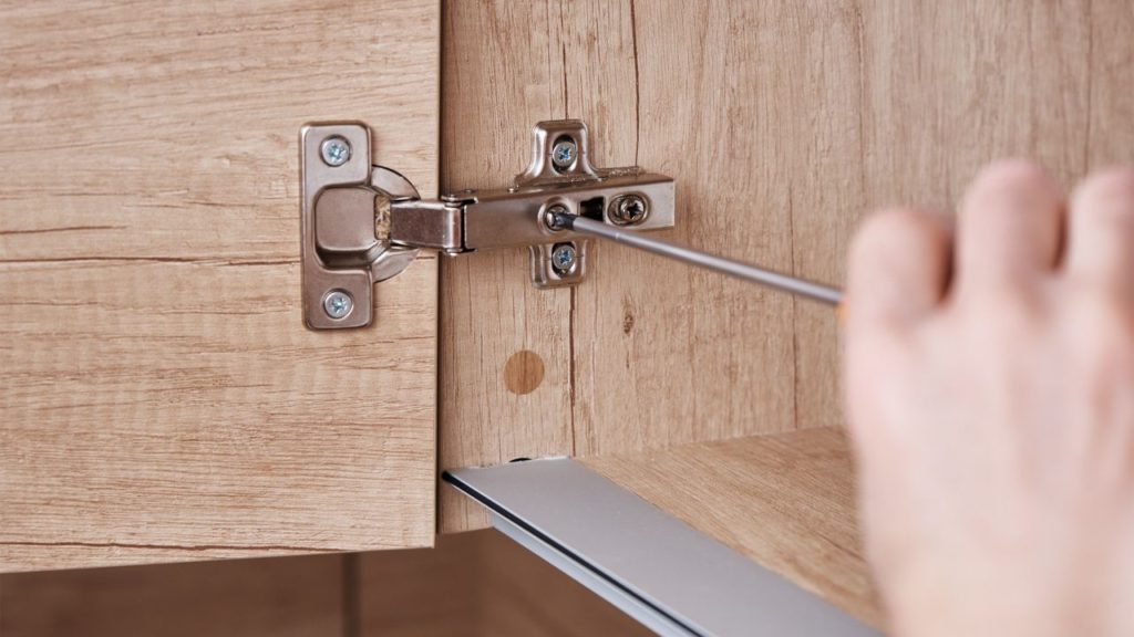 A person adjusting the side or horizontal position of a cabinet door.