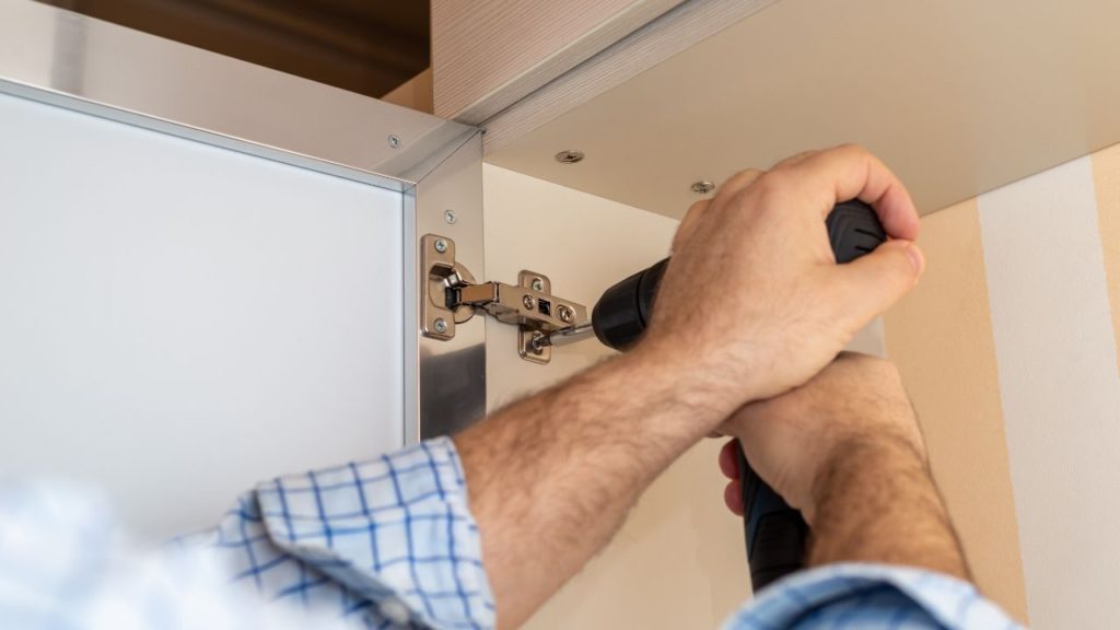 A person using an electric screwdriver to adjust the cabinet door's height.