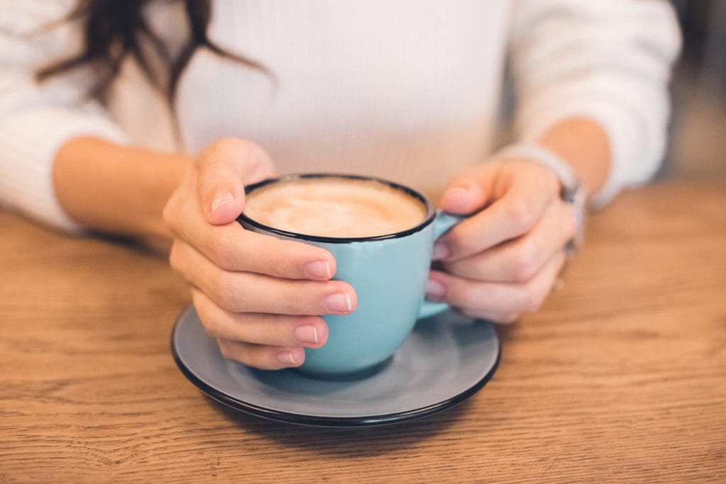 cropped image of woman sitting with coffee cup at table in cafe