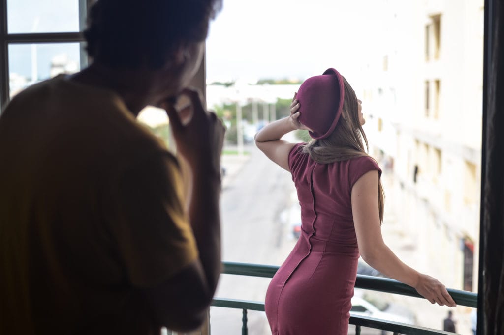 Man admiring beautiful lady in fitted dress standing on balcony