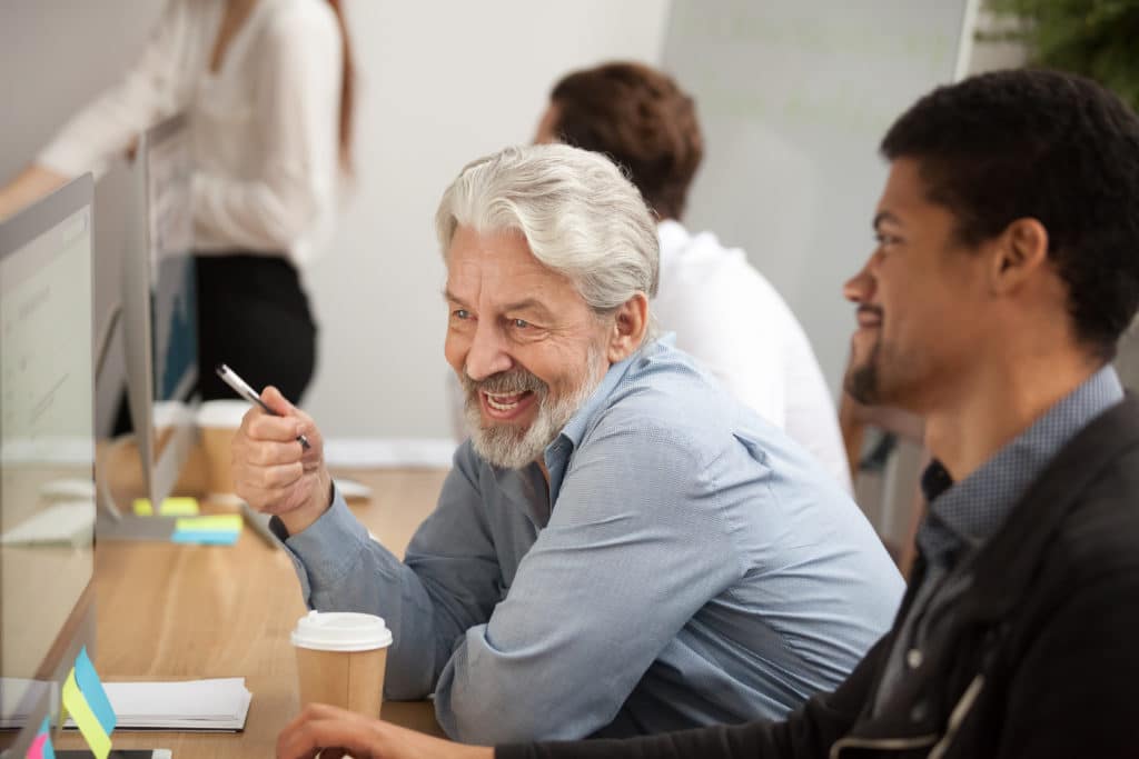 Smiling,senior,employee,discussing,email,with,african,colleague,at,workplace,