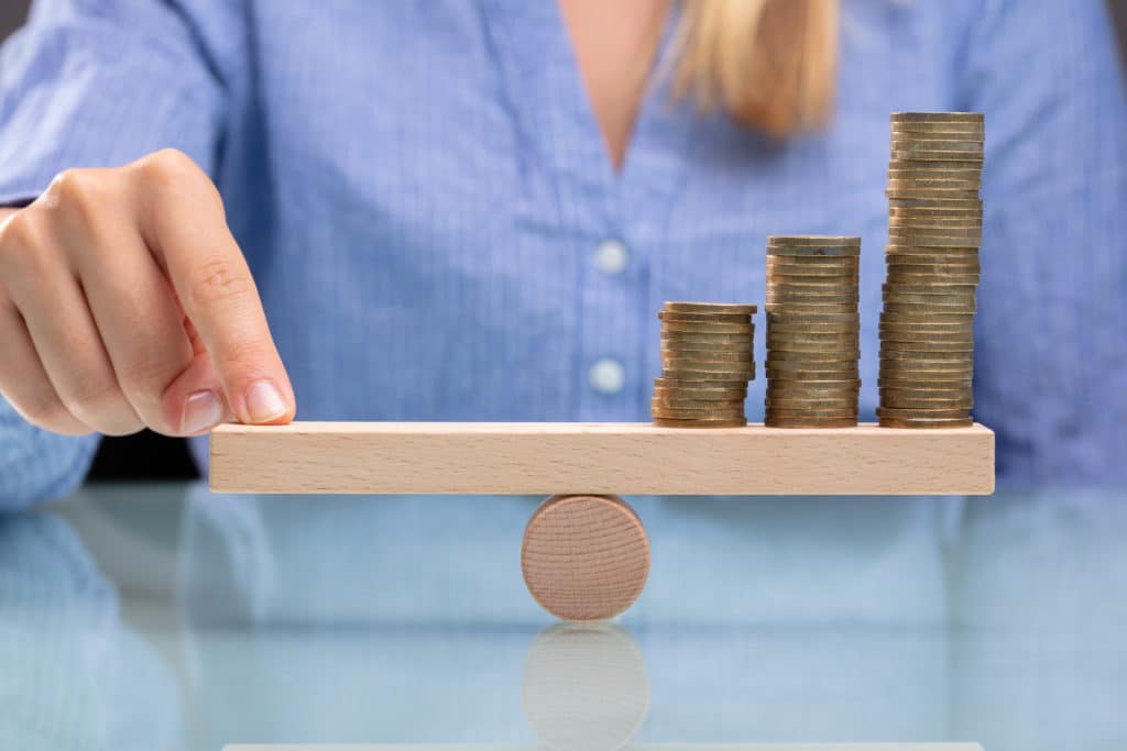 Businesswoman,balancing,stacked,coins,with,finger,on,wooden,seesaw