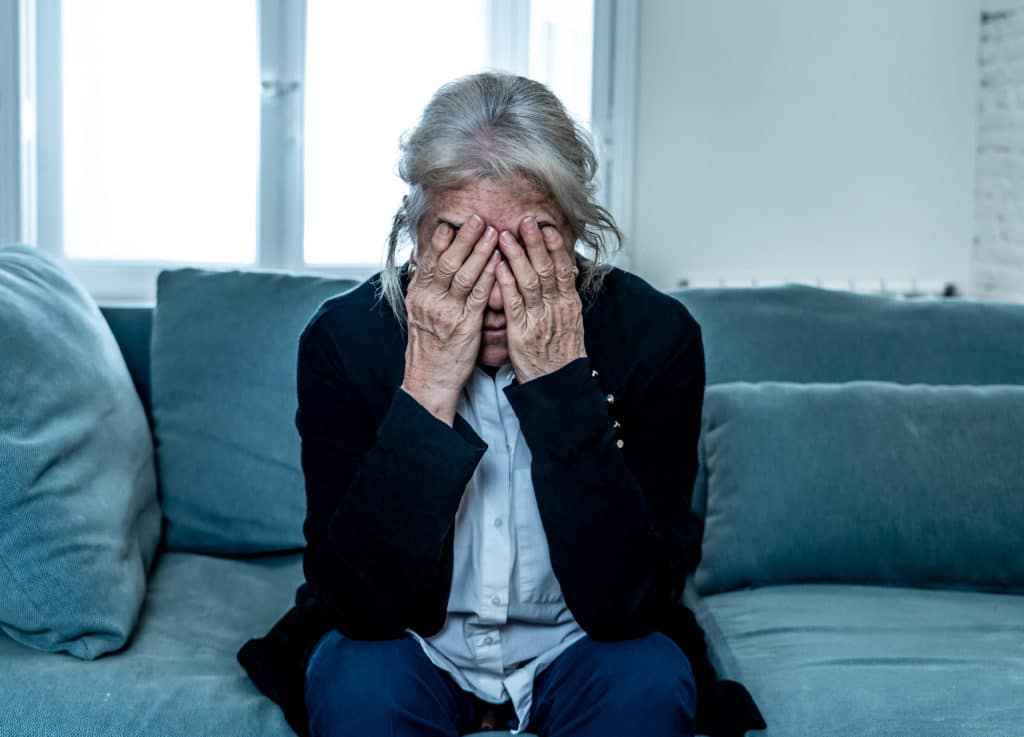 Lonely depressed senior old widow woman crying on couch in retirement