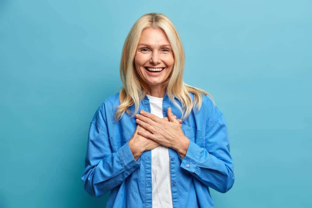 Thankful Middle Aged Woman Presses Hands To Chest Smiles Broadly