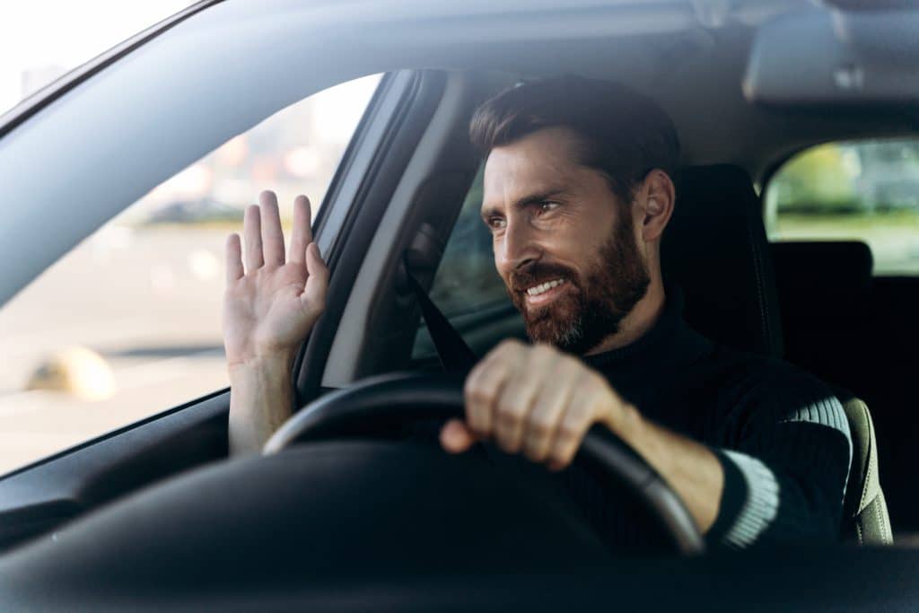 Handsome,young,smiling,driver,of,car,waving,hand,as,a