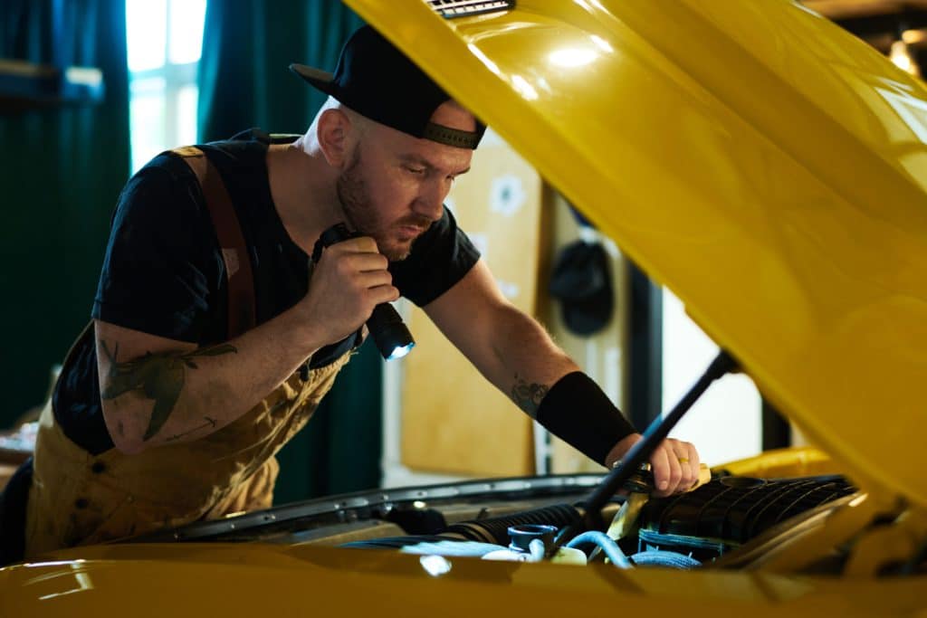 Young,mechanic,of,car,repair,workshop,checking,engine,of,yellow