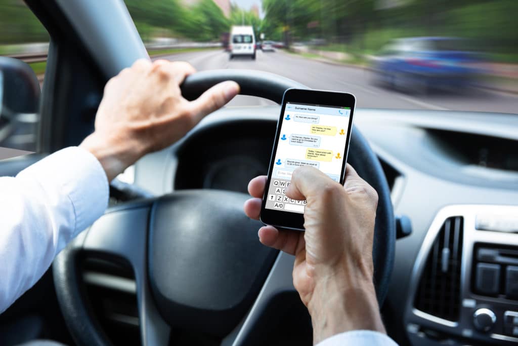 Man Typing Text Message On Mobile Phone While Driving Car