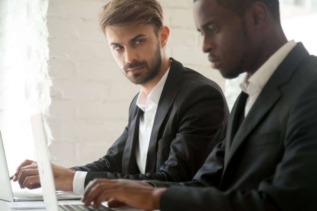 Suspicious Cunning Male Caucasian Worker Looking At Serious Working African