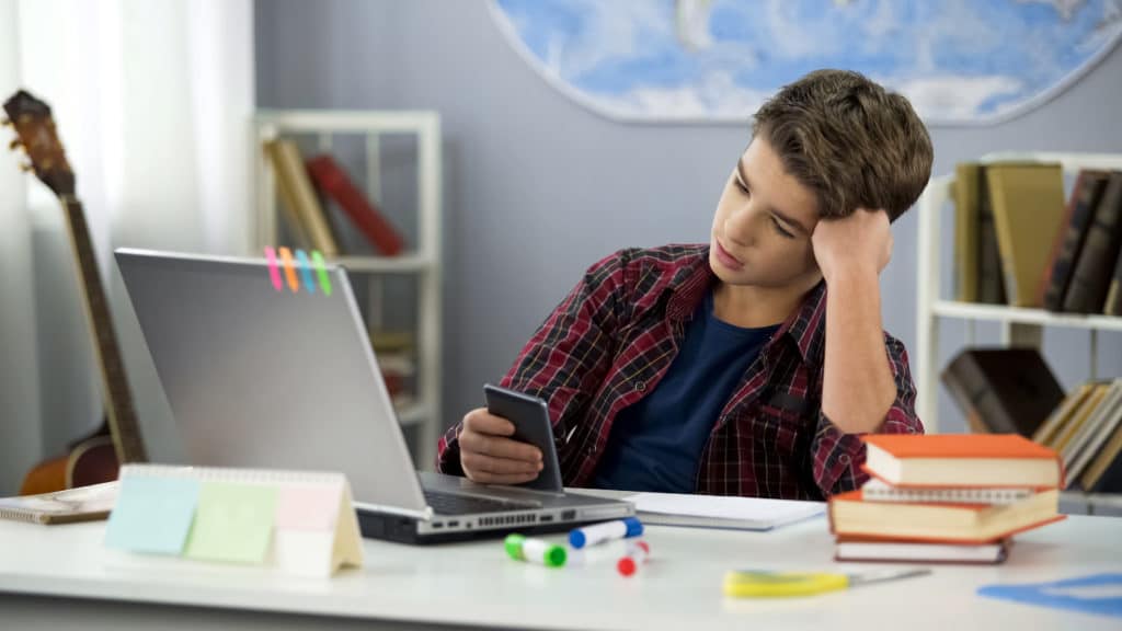 Bored Guy Scrolling Apps On Phone Distracted From Homework Procrastination