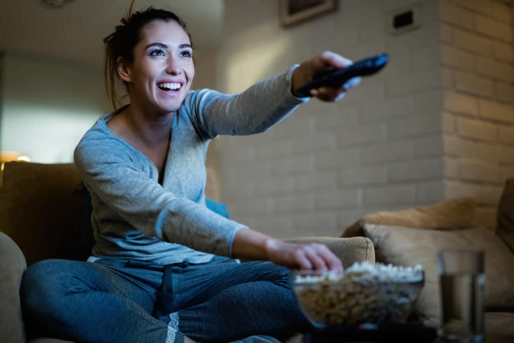 Young Happy Woman Changing Channels With Remote Control While Watching