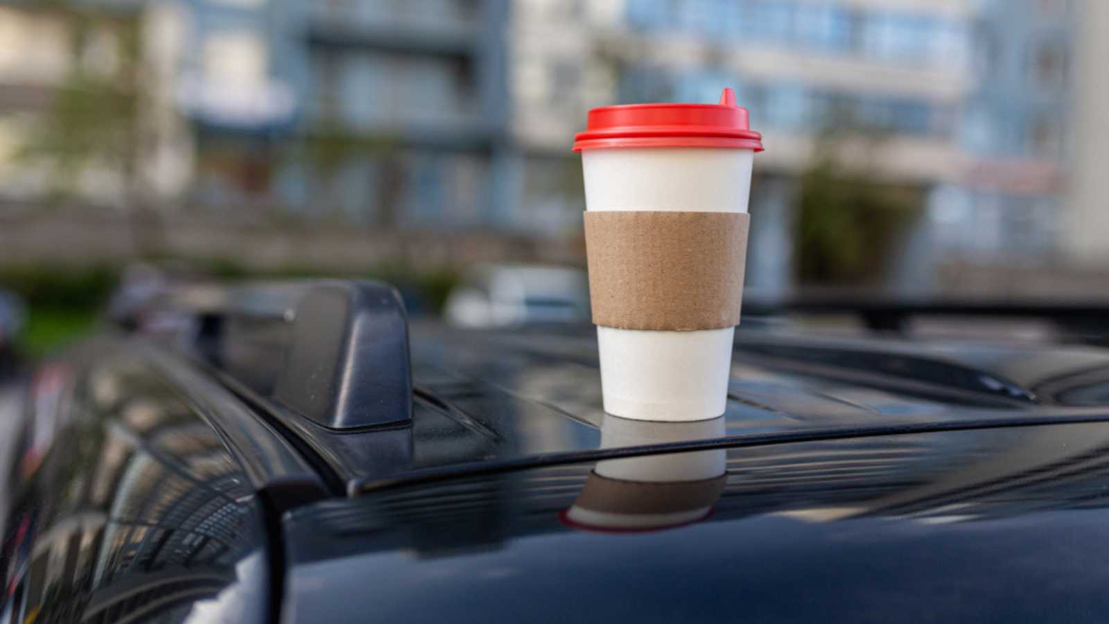 White paper coffee Cup with red lid on car roof. Paper Cup with hot tea on the roof of the SUV close up on the background of the windshield
