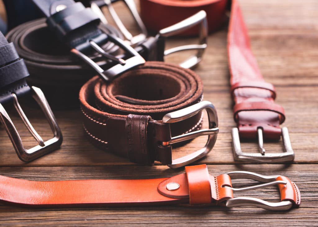 Collection Of Leather Belts On A Wooden Table. Leather Colored
