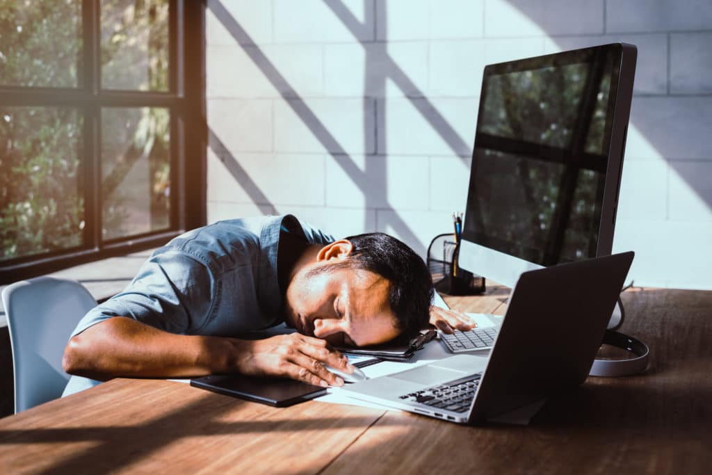 Tired Young Asian Man Sits Asleep At The Computer Desk.