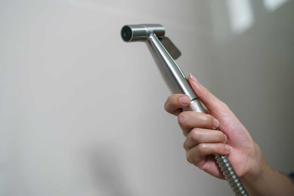 Woman Hand Using Chromium Bidet Shower Sitting On Toilet.