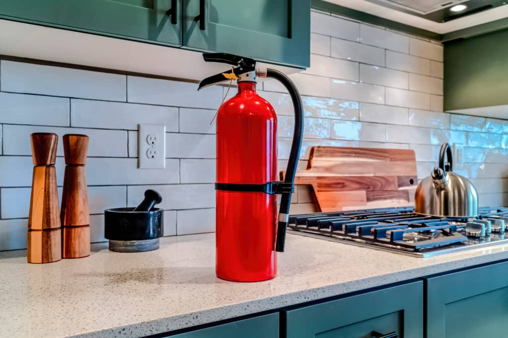 Red Fire Extinguisher Beside Cooktop On The Countertop Inside Kitchen
