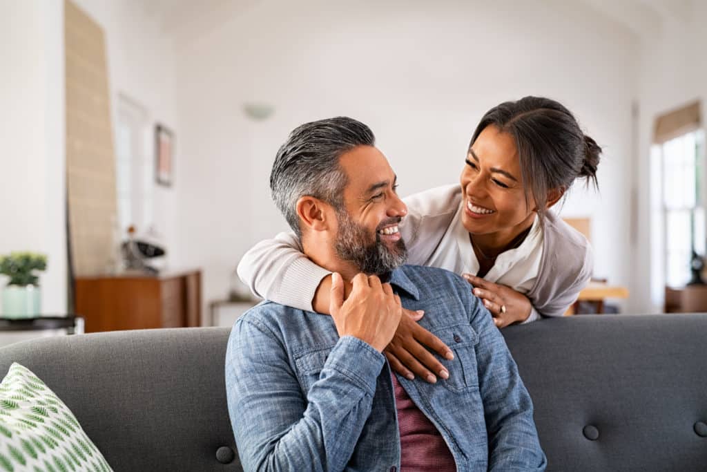 Smiling Ethnic Woman Hugging Her Husband On The Couch From