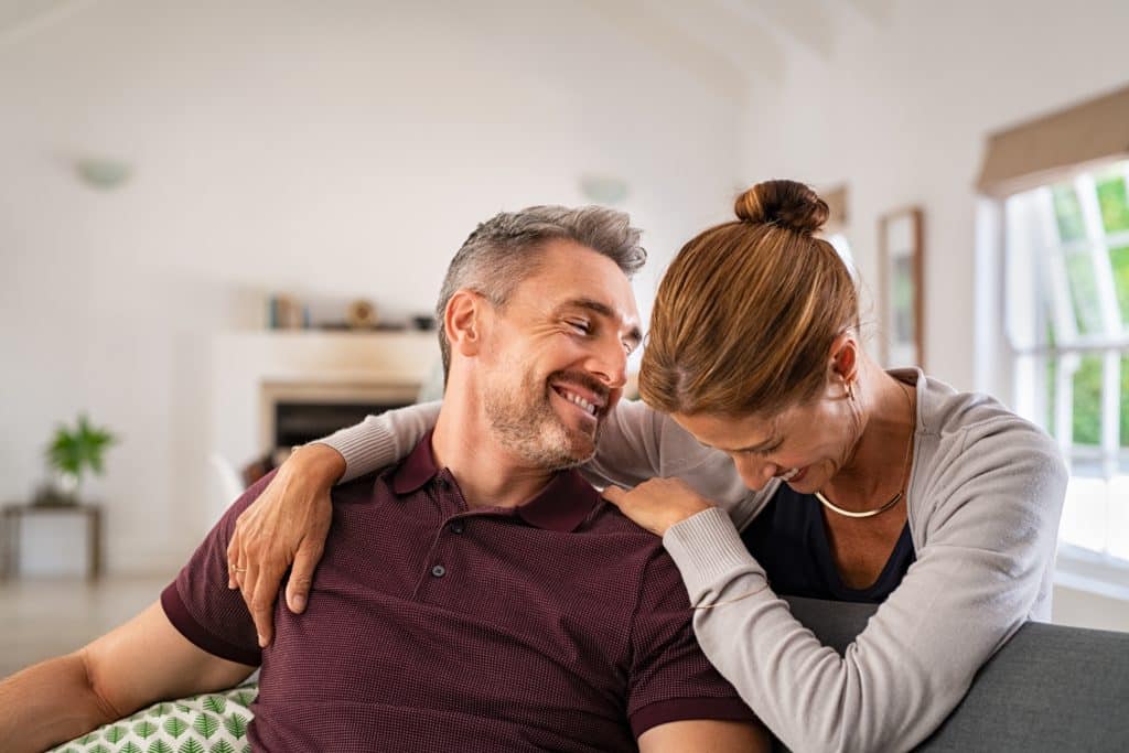 Happy Mature Couple Embracing On Sofa While Laughing. Middle Aged