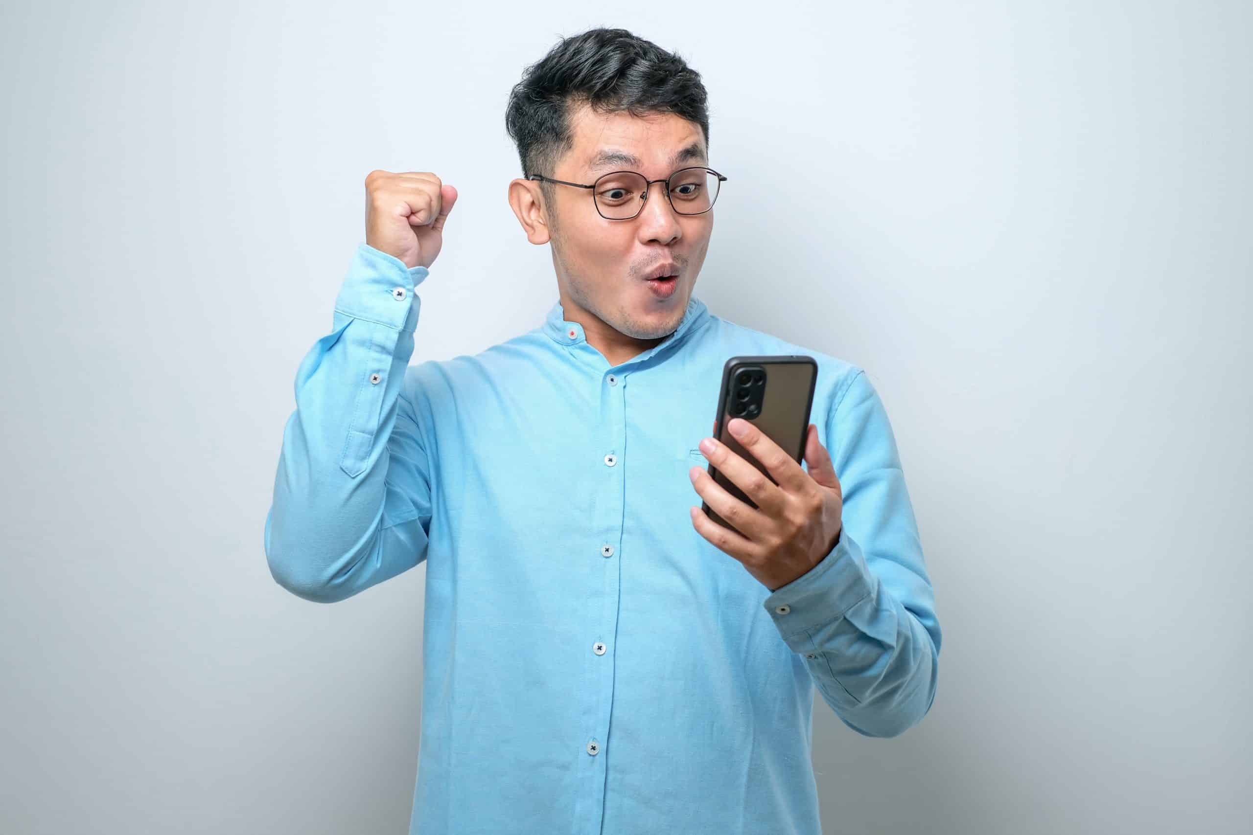 Shocked Young Good Looking Asian Man Using Smartphone To Read