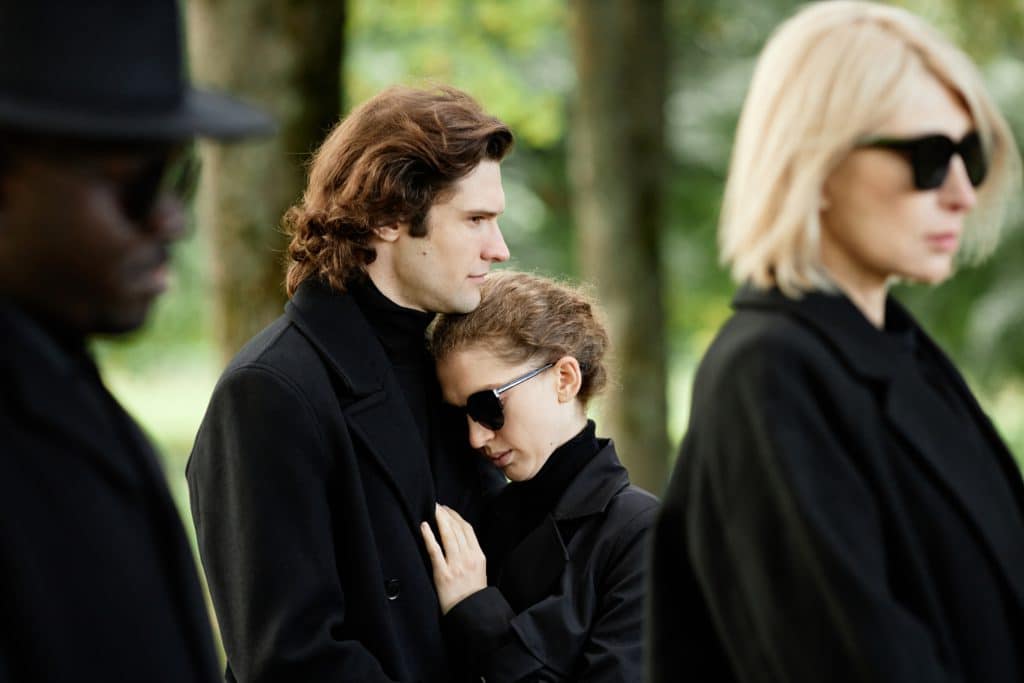 Portrait Of Young Couple Wearing Black Grieving Together And Embracing