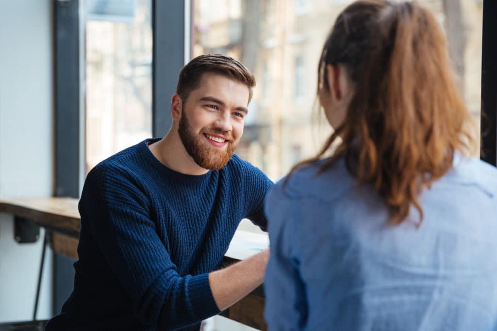 Happy Young Couple Talking And Drinking Coffee Near The Window