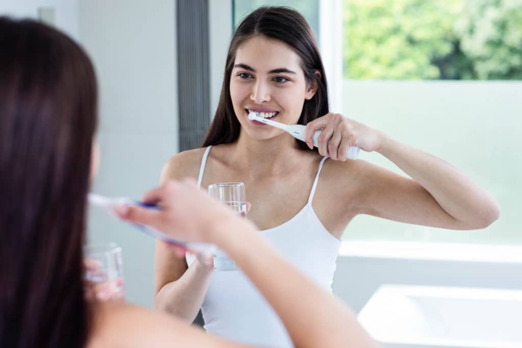 Smiling Brunette Brushing Teeth In Bathroom