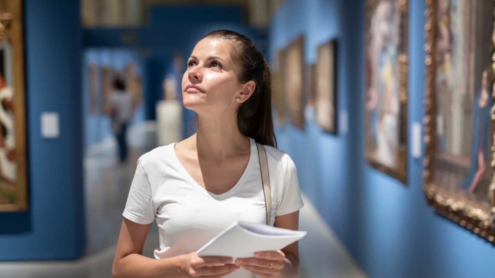 Young woman with guide brochure looking at artworks in museum
