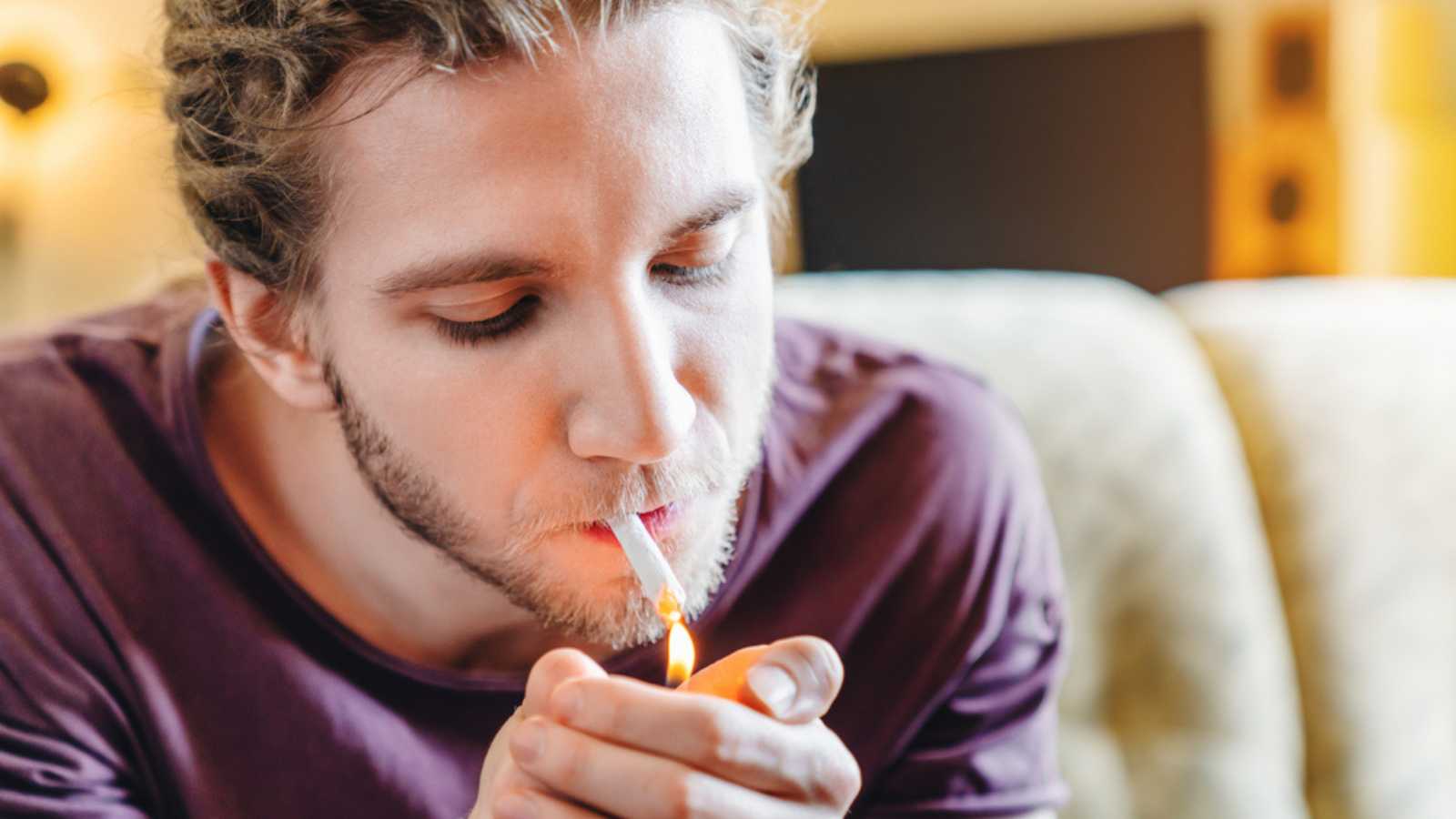 Young caucasian man smoking cannabis weed at home and using his lighter

