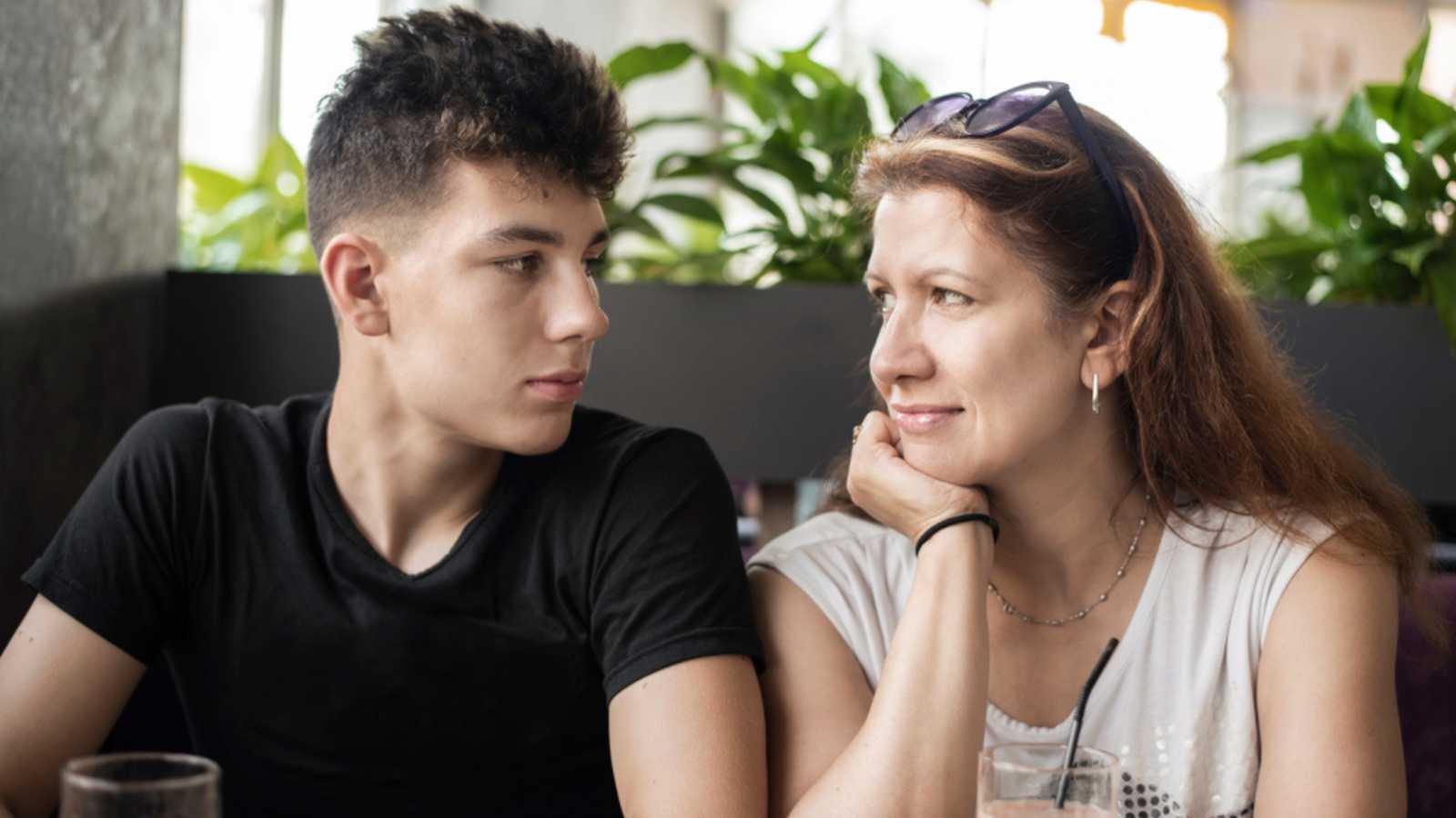 Pretty woman sitting with her teenage son in a cafe and talking - son looking lovingly at mom. The concept of communication between parents and children