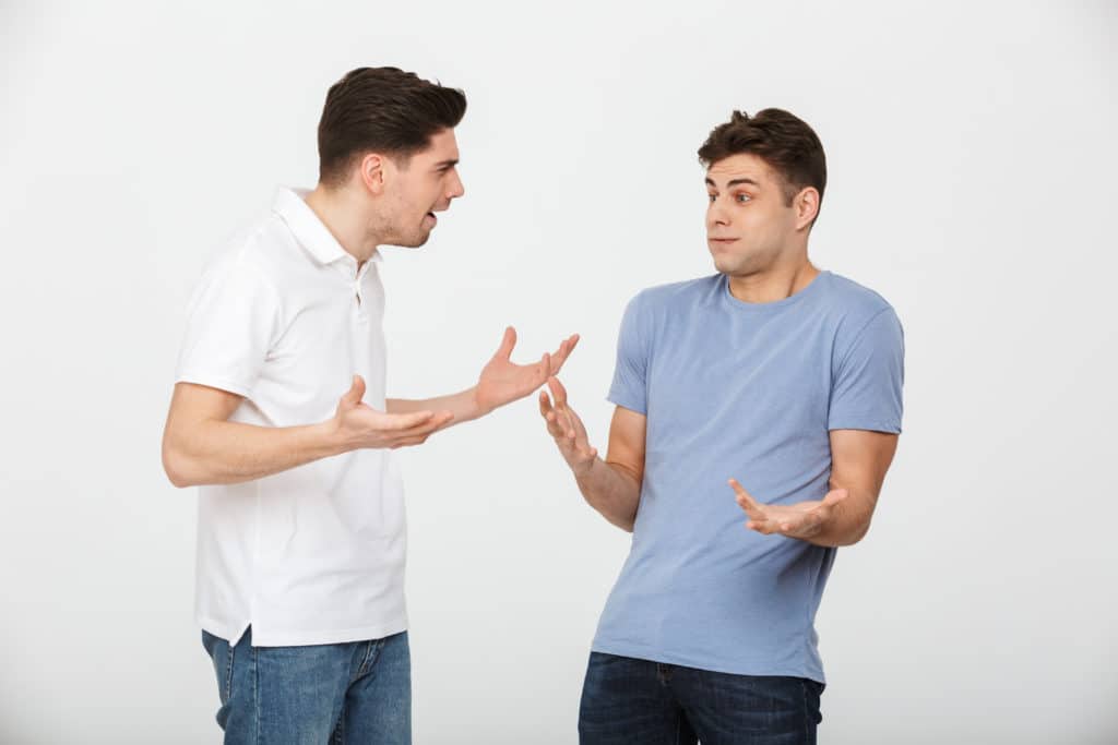 Portrait Of Two Confused Young Men Talking Isolated Over White