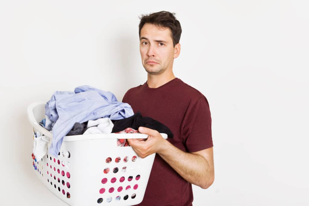 Frustrated Young Man Holding Basket Full Of Clothes. Laundry Time