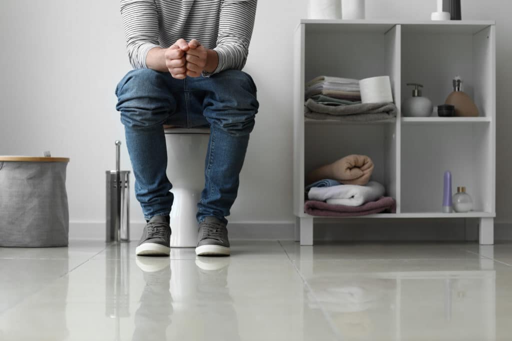 Man Sitting On Toilet Bowl At Home