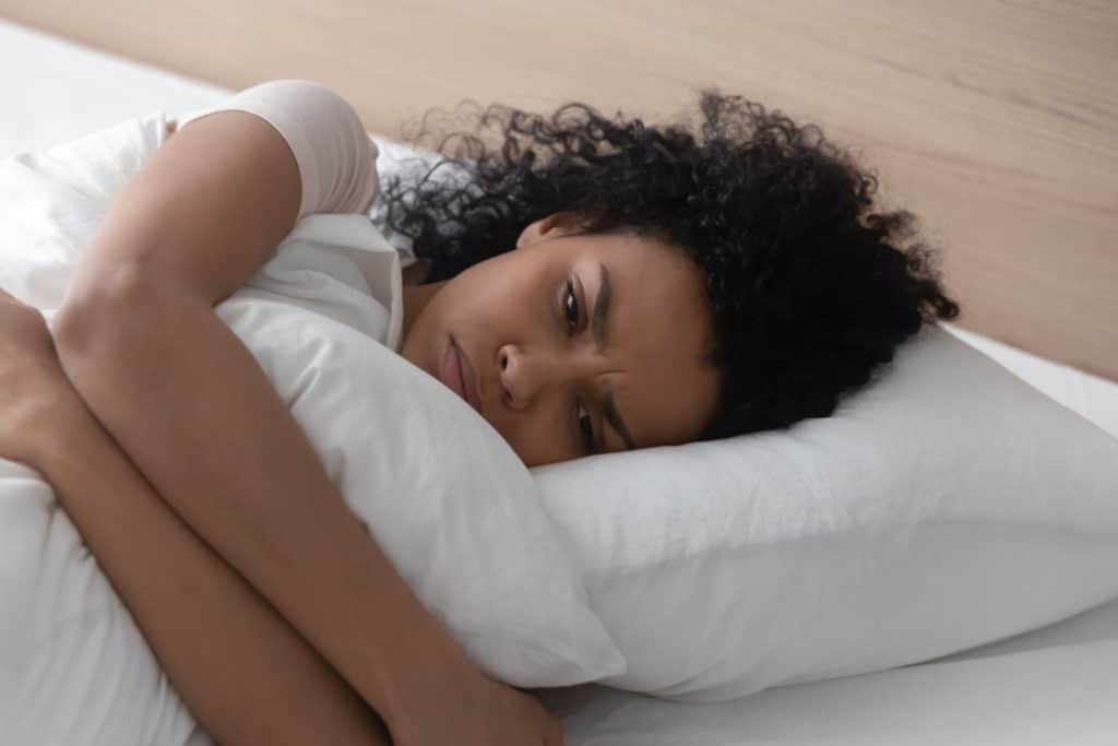 Sad Depressed African American Young Woman Hugging Pillow Lying In