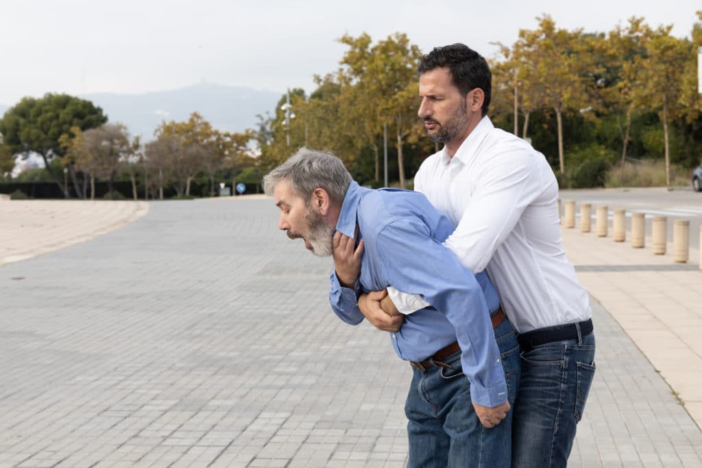 Man Doing The Heimlich Maneuver To An Old Man With