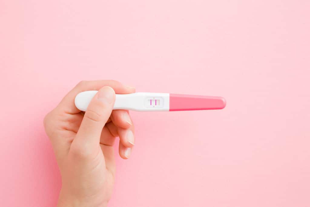 Young Woman Hand Holding Pregnancy Test With Two Stripes. Pastel