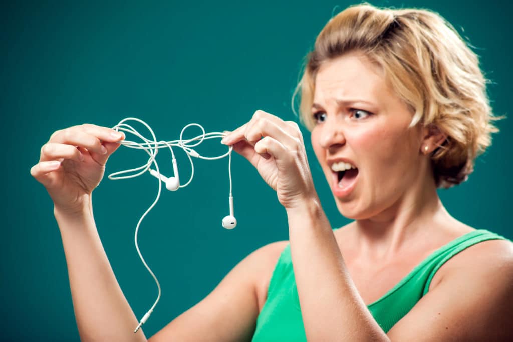 Angry Woman Holding White Tangled Earphone Trying To Untangle It.
