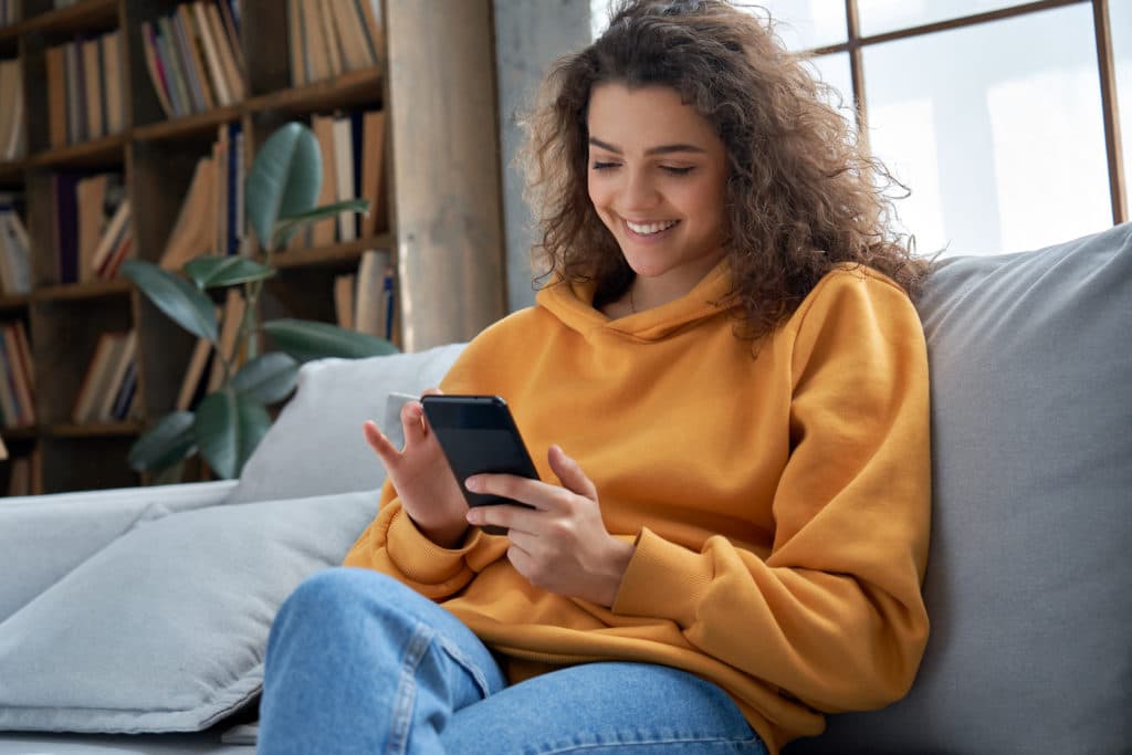 Happy Millennial Hispanic Teen Girl Checking Social Media Holding Smartphone