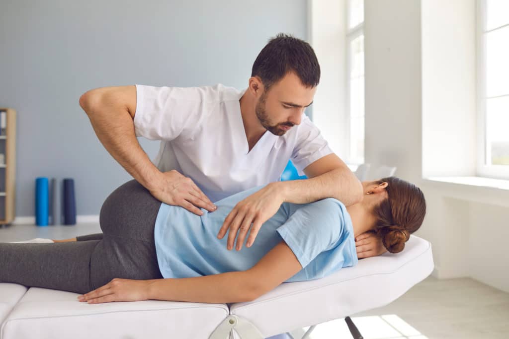 Young Man Doctor Chiropractor Or Osteopath Fixing Lying Womans Back