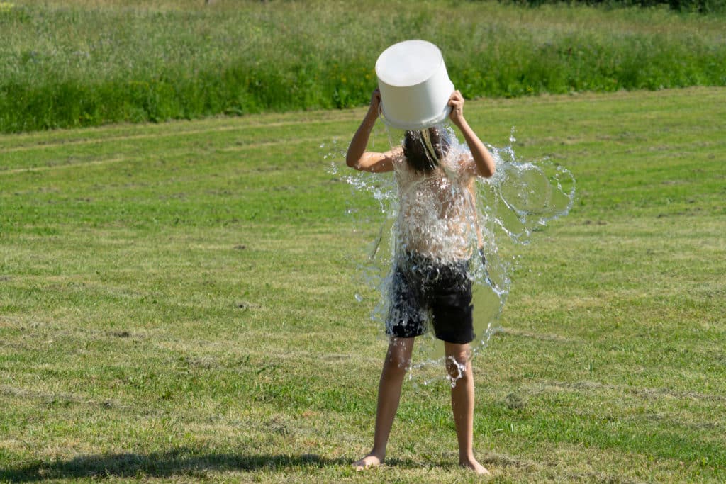 Teenage Boy Pouring Bucket Of Cold Water Over His Head