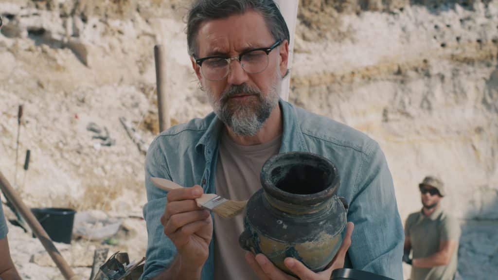 Mature Archaeologist Discussing Antique Vessel With Colleague