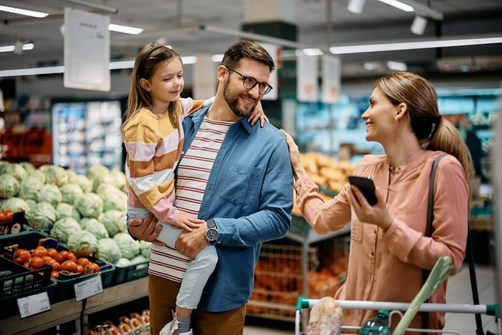 Happy Parents With Daughter Communicating While Buying At Supermarket.