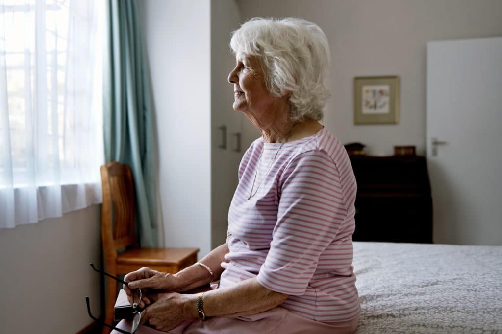 A Solemn Elderly Woman Sitting On Her Bed Dealing With