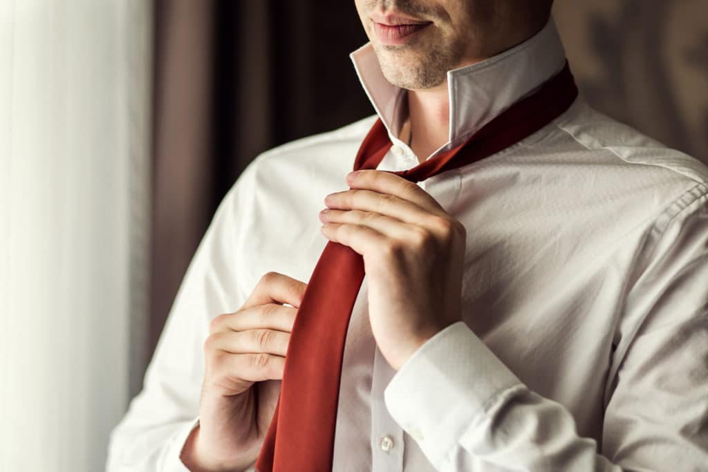 Man In Shirt Dressing Up And Adjusting Tie On Neck