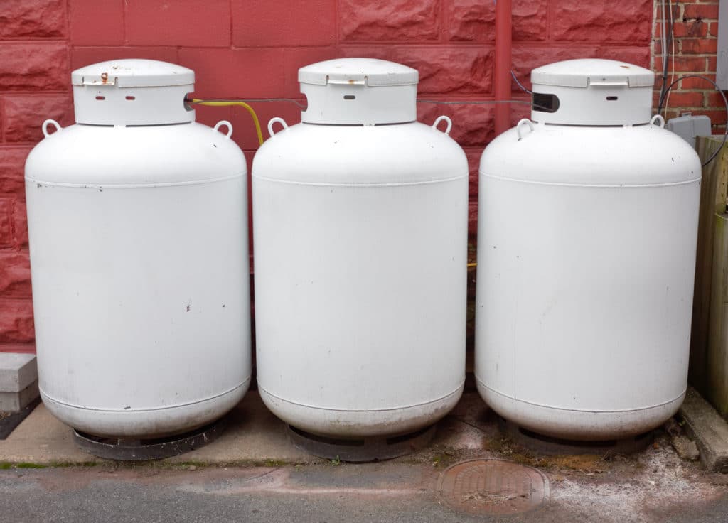 Three White Industrial Propane Tanks Against Red Stone Wall.