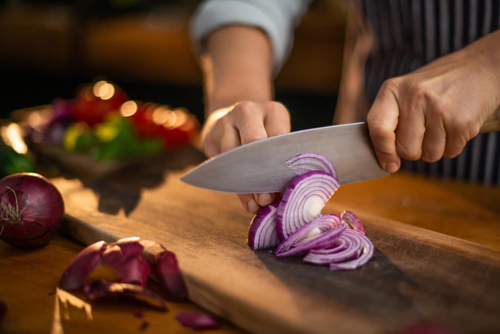 Female Chef Is Precisely Slicing Red Onions On A Wooden
