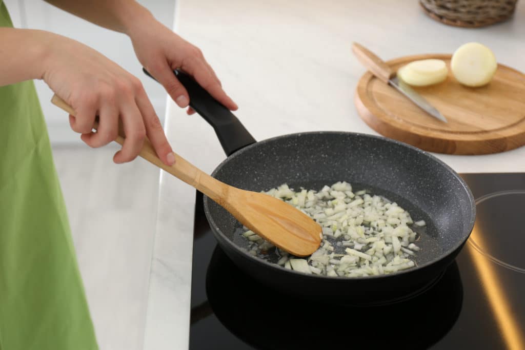 Woman Frying Chopped Onion In Kitchen Closeup