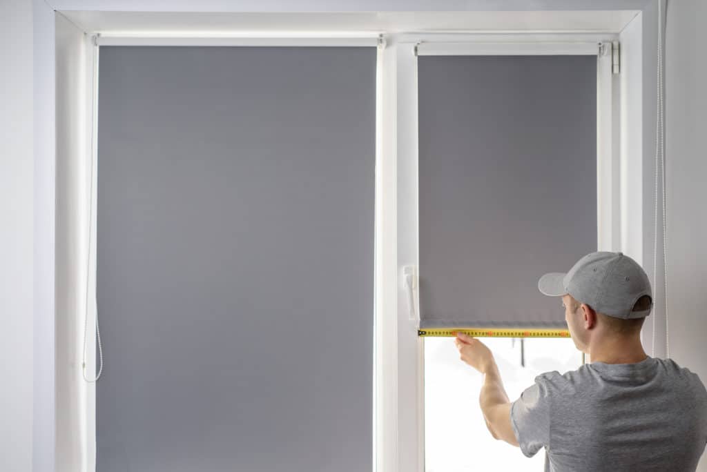 Man Installing Gray Roller Blinds On The Window