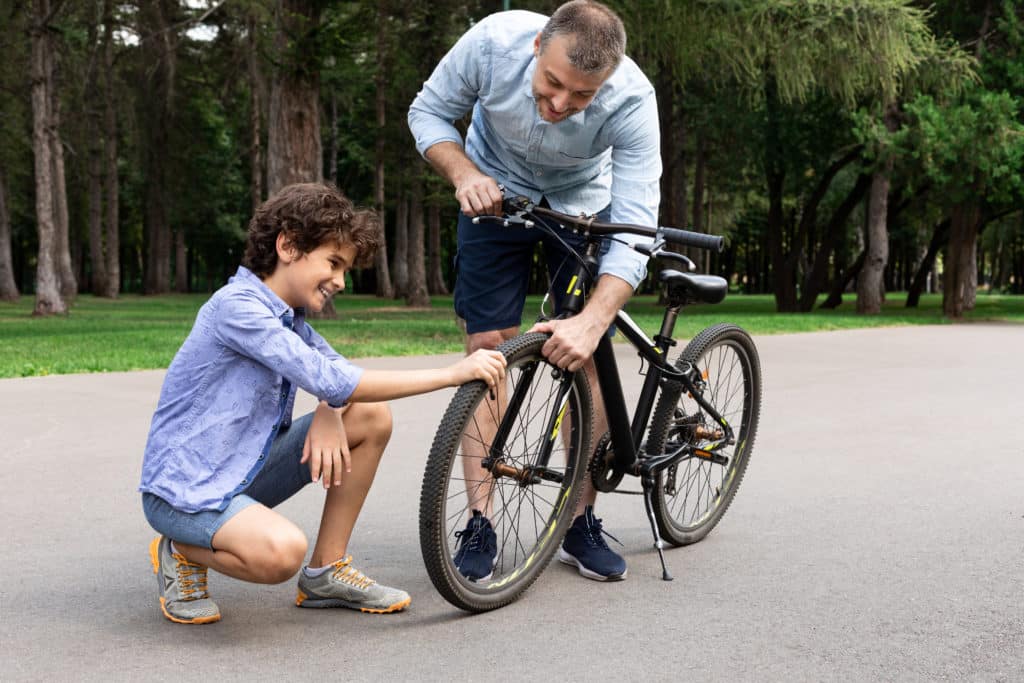 Portrait Of Smiling Adult Father And Son Checking Tire Of