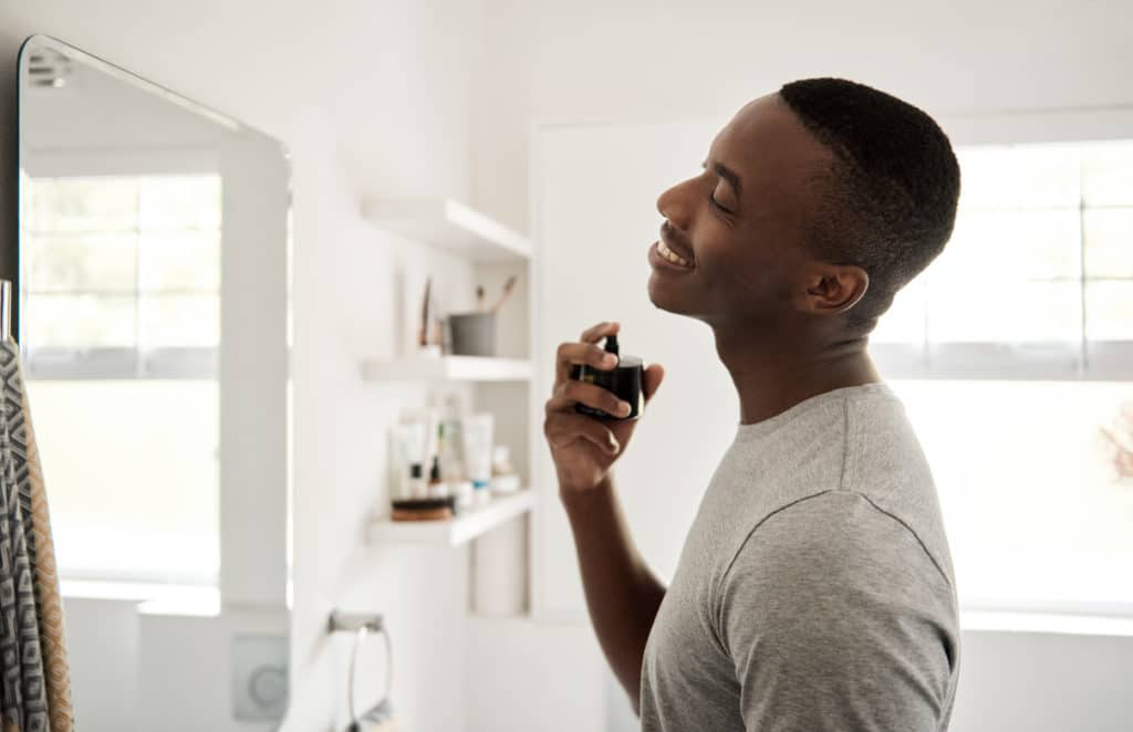 Smiling Young African Man Spraying On Cologne In His Bathroom
